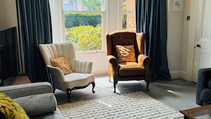 A living room with a sofa, two armchairs, a coffee table, and a view of greenery through large windows. - Spacious family-friendly & pet-friendly Victorian home in bustling east Belfast (Belfast)