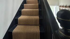Un escalier recouvert d’une moquette à motifs, une tête de cerf décorative fixée au mur et une fenêtre laissant entrer la lumière naturelle.