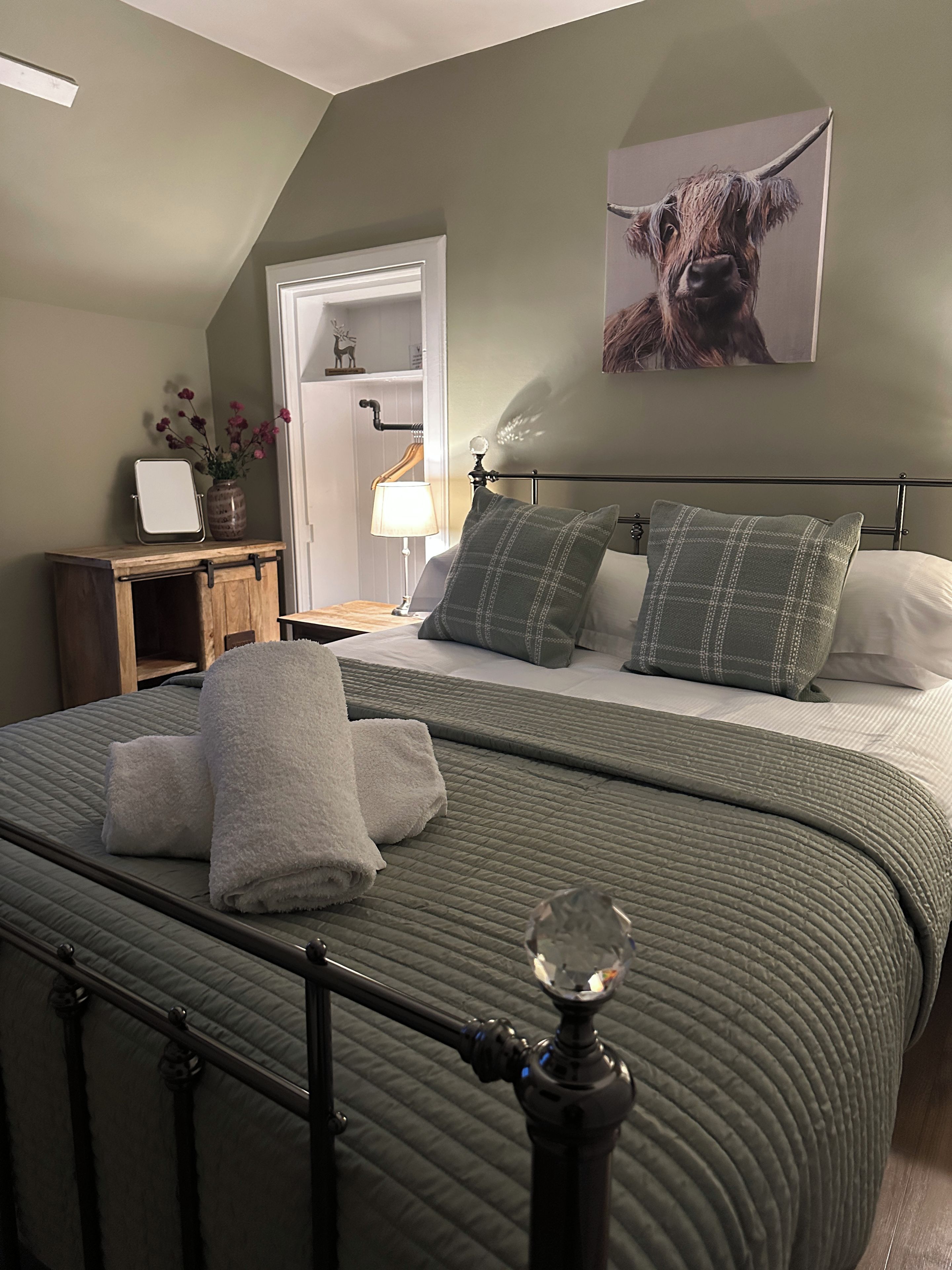 Ein Schlafzimmer mit Bett, Kissen, Nachttisch, Lampe, Spiegel, Kommode und Tür.