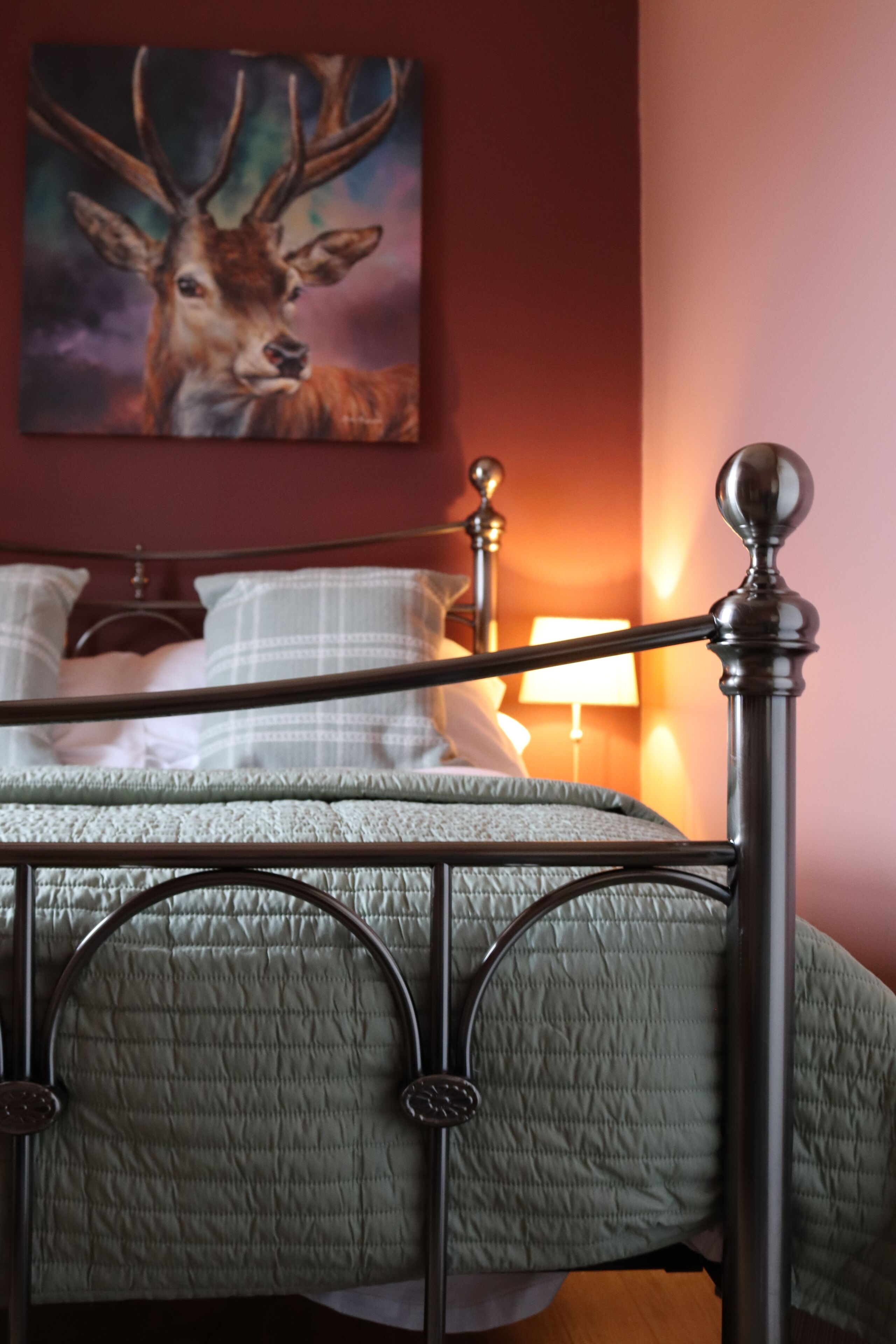 Uma cama com estrutura de metal, um edredom verde e um quadro de um veado na parede.