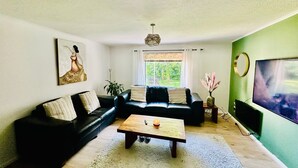 Una sala de estar con un sofá seccional, una mesa de centro, un televisor y una ventana con cortinas.