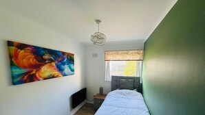 Un dormitorio con una cama, un cuadro abstracto lleno de color, una ventana con vistas y una lámpara en el techo.