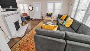 Una sala de estar con chimenea, un sofá gris, cojines amarillos y un televisor.