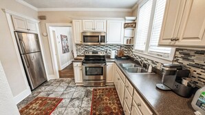 Una cocina con armarios blancos, electrodomésticos de acero inoxidable, salpicadero de azulejos y encimera de granito.
