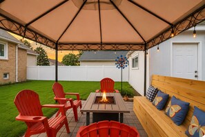 Un espacio de patio cubierto con un brasero, sillas rojas y un banco de madera con cojines de diseño de mariposa.