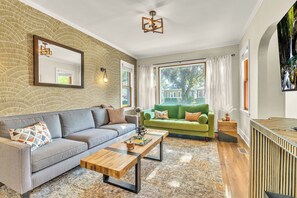 A modern living room with a grey sofa, a wooden coffee table, a green sofa, and a large window with curtains. - Sleeps 10 + Coffee bar + Game Room + Train to CHGO - Holiday Home (Brookfield)