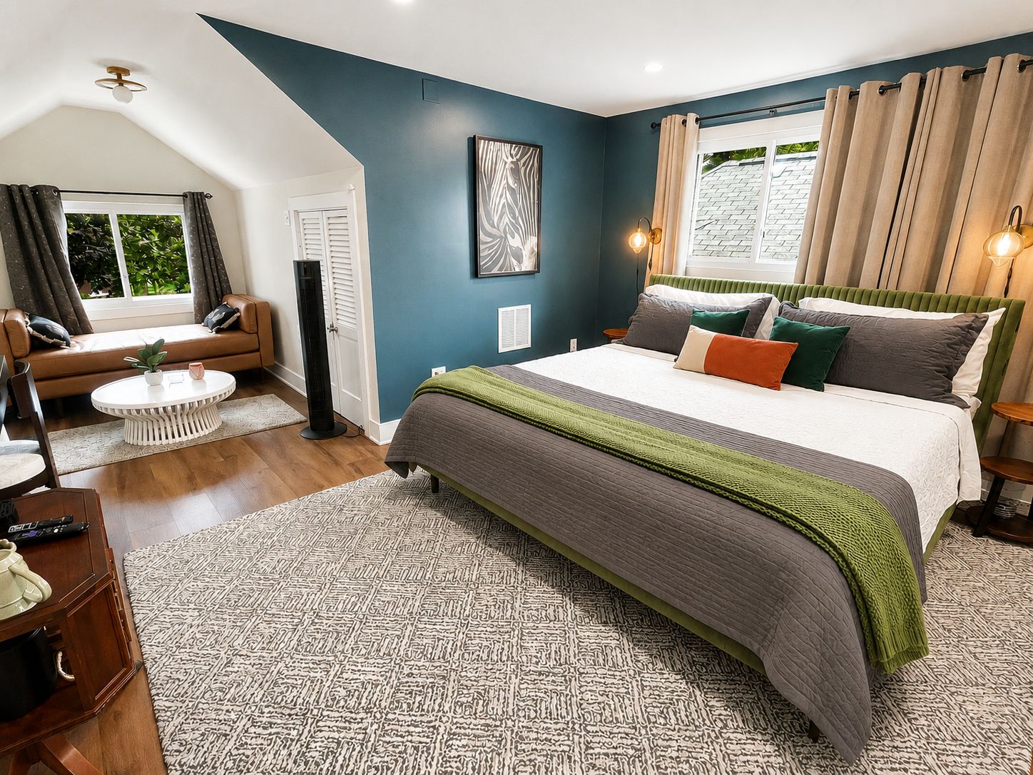 Ein Schlafzimmer mit einem großen Bett, einem Schlafsofa, einem runden Couchtisch und einem Fenster mit Vorhängen.