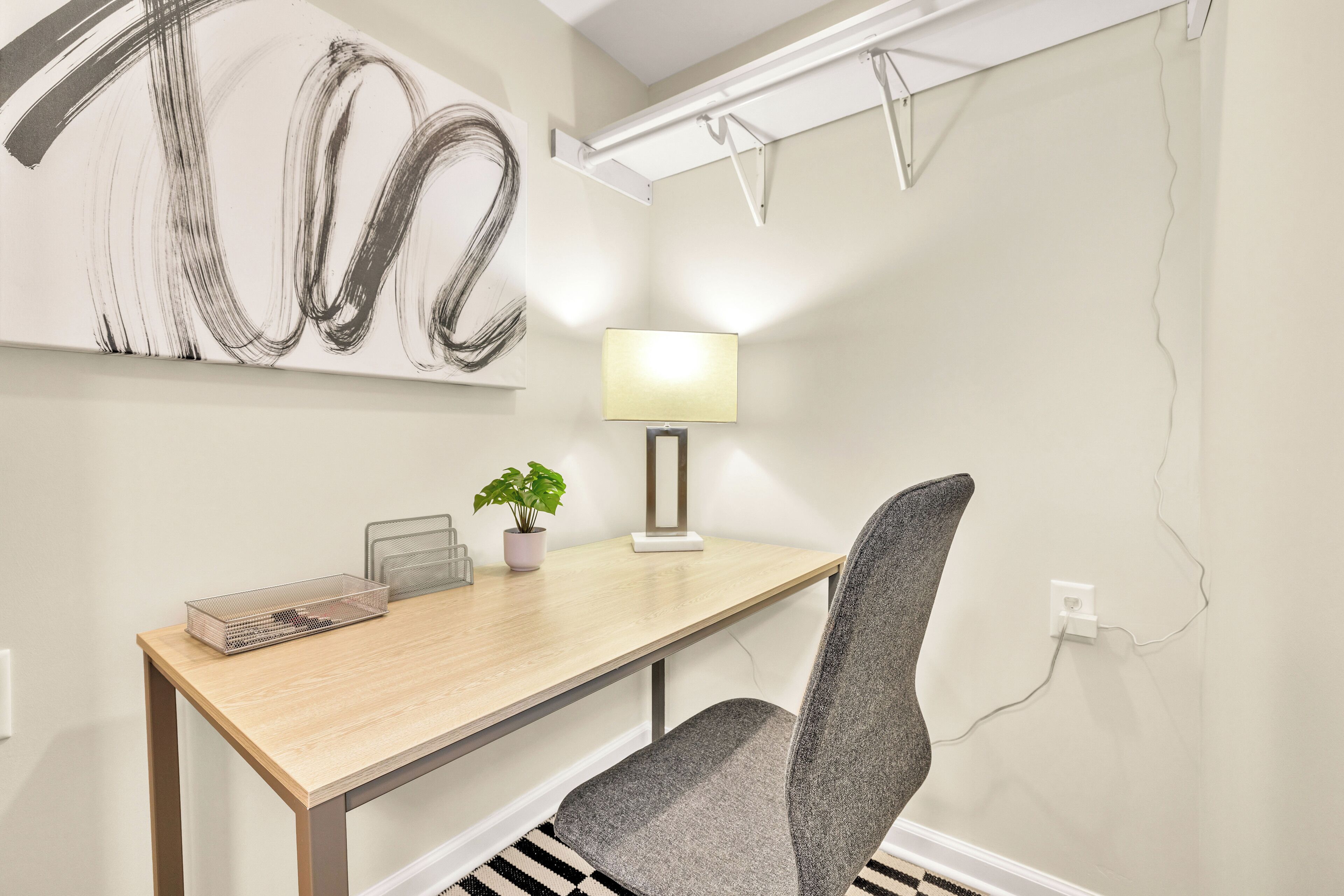 A modern office space with a wooden desk, a grey office chair, a potted plant, and a wall-mounted lamp.