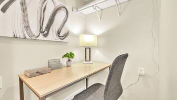 A modern office space with a wooden desk, a grey office chair, a potted plant, and a wall-mounted lamp.
