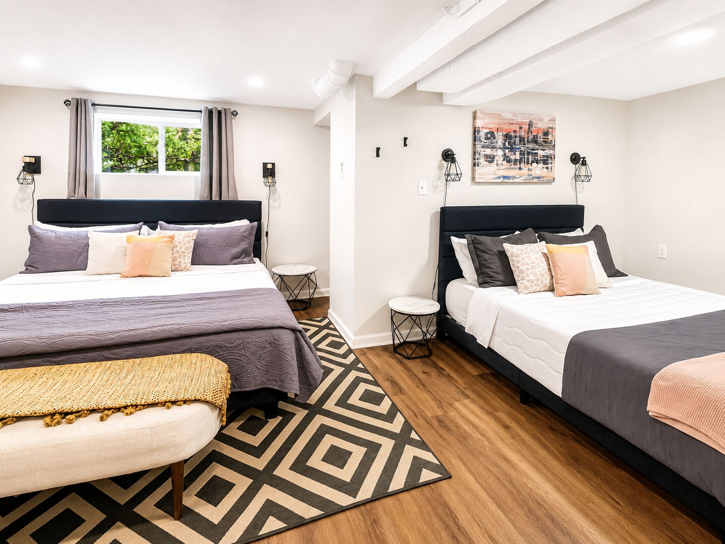 A hotel room with two beds, a window with curtains, a small round table, and a geometric patterned rug.