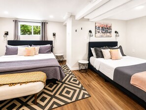 A hotel room with two beds, a window with curtains, a small round table, and a geometric patterned rug.