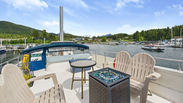A boat deck with seating, a table, and a view of a marina and mountains.
