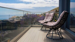 A balcony with two cushioned chairs, a glass railing, and a view of the sea and buildings. - White Apartment (Funchal)