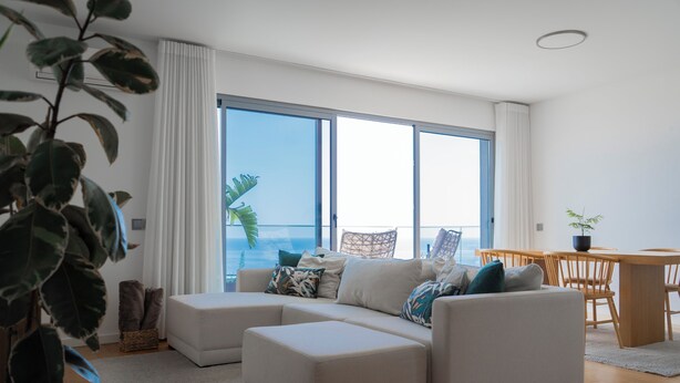 A modern living room with a sectional sofa, a dining table, and a large window overlooking the sea. - White Apartment (Funchal)