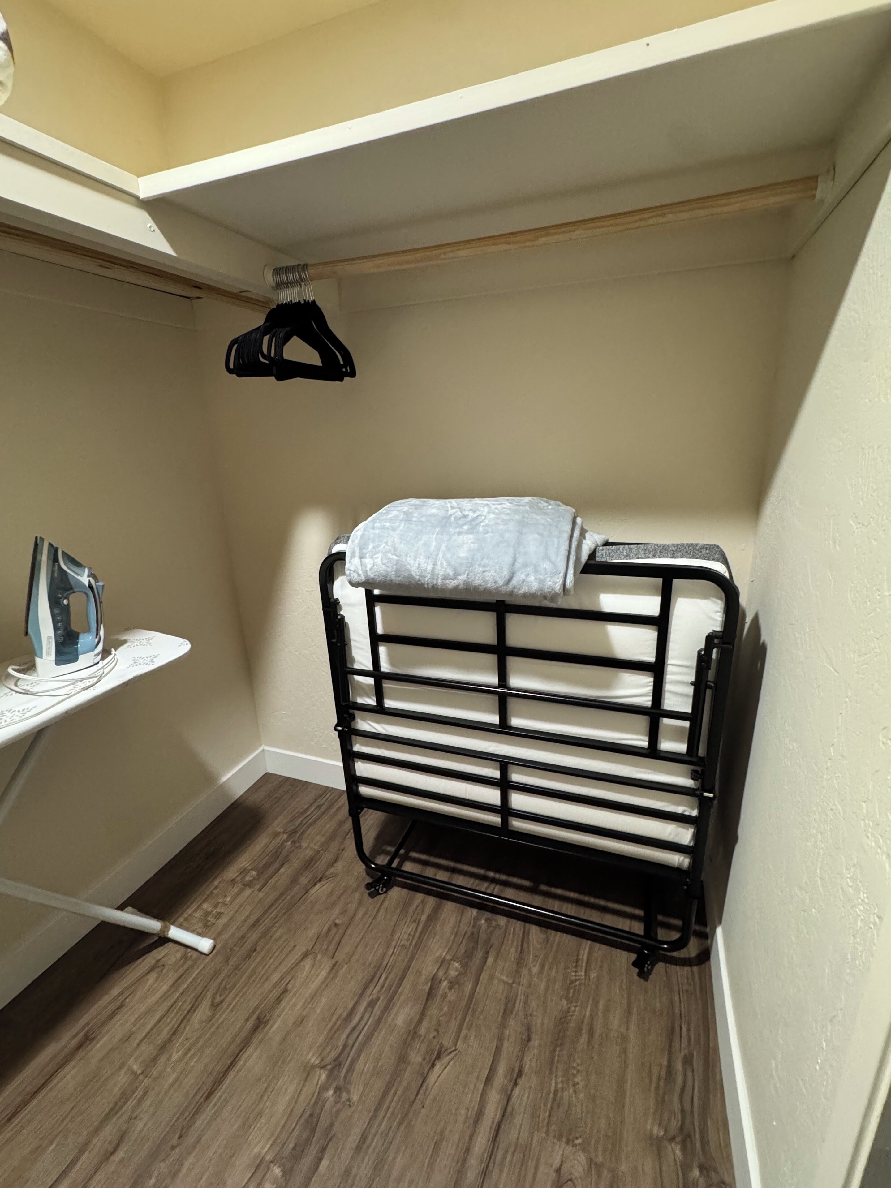 A small, narrow room with a metal drying rack, a shelf with an iron, and a hanging rack.