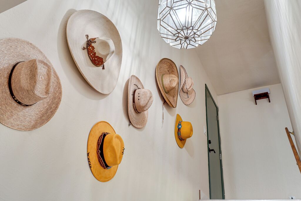Une pièce dont un mur blanc est orné de différents chapeaux, et où un grand couteau est appuyé contre le mur.