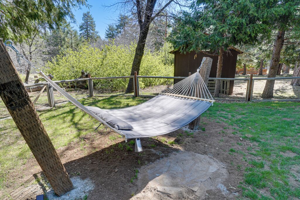 A hammock in a natural setting with trees and a wooden structure in the background.