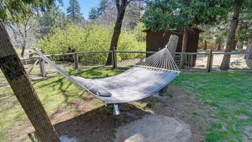 A hammock in a natural setting with trees and a wooden structure in the background.