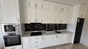 A modern kitchen with white cabinets, a black countertop, a built-in oven, a gas stove, and a black refrigerator.