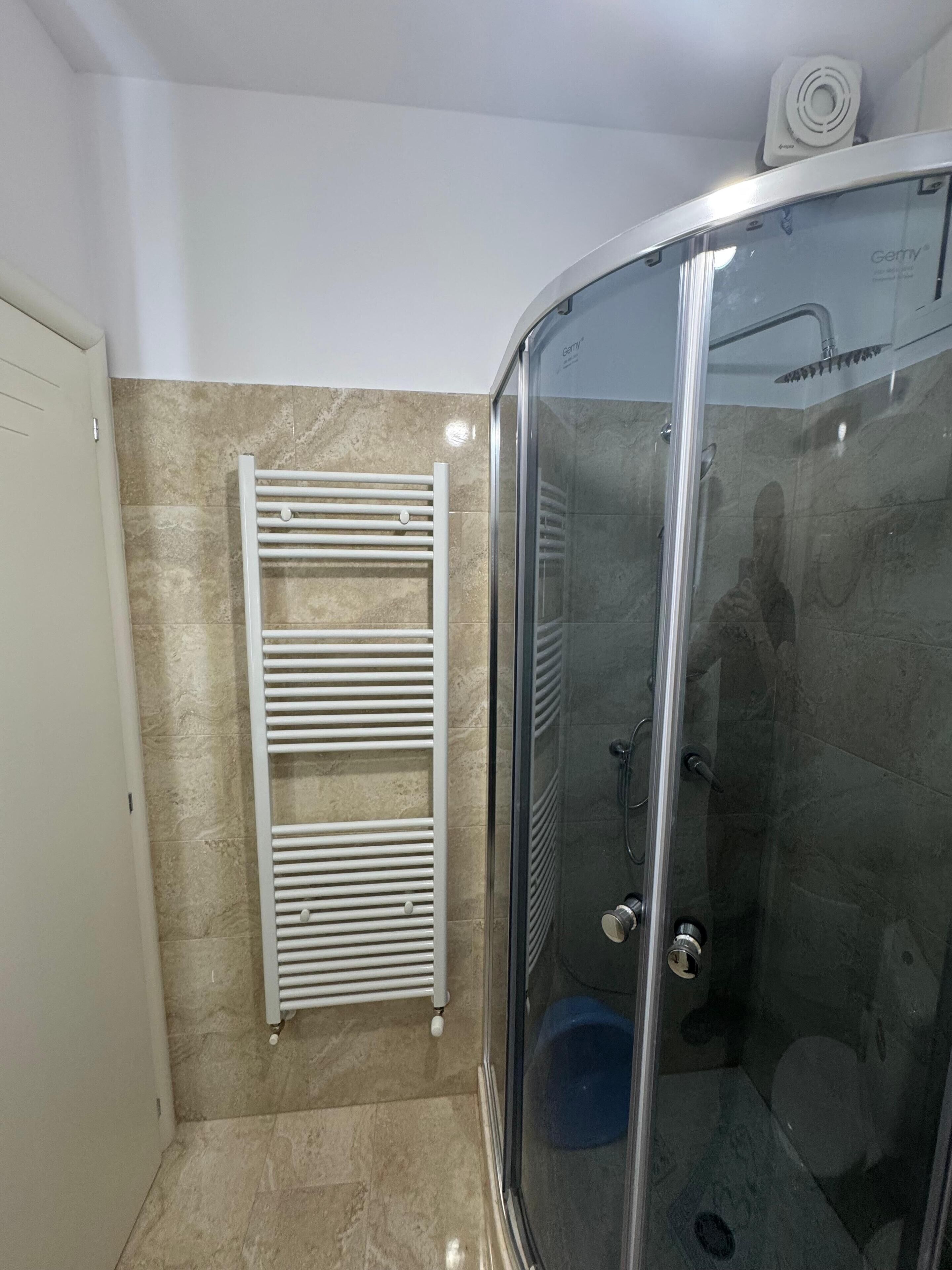 Une douche fermée par des parois de verre, avec un porte-serviettes blanc adossé à un mur carrelé.
