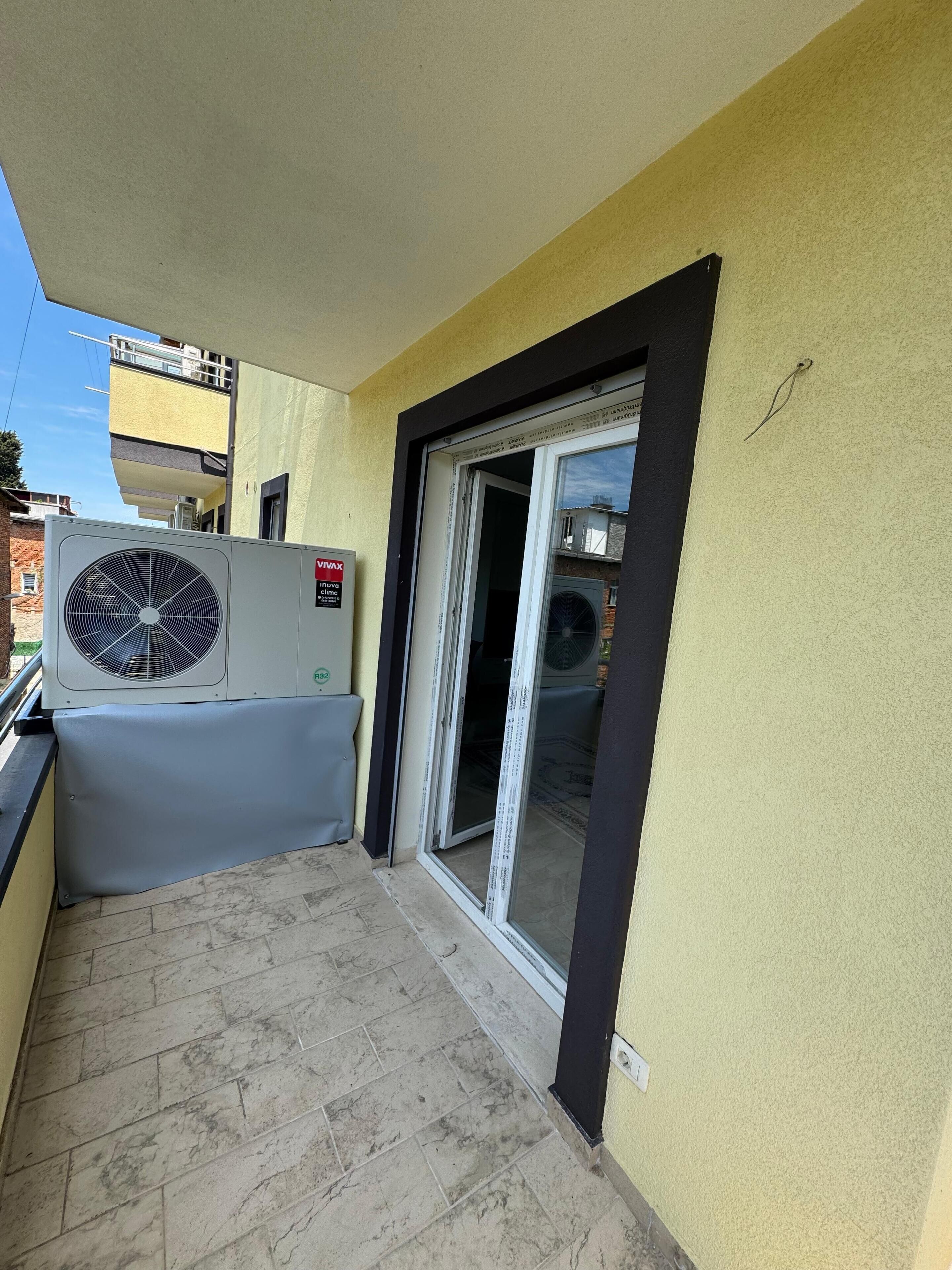 An outdoor balcony with a large air conditioning unit, a sliding glass door, and a tiled floor.