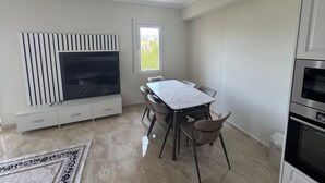 A modern kitchen with a dining area, white cabinetry, a built-in stove, and a large window.