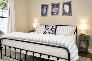 A neatly made bed with striped bedding, two bedside lamps, and three framed wall art pieces above it. - Gritz & Giggles, Southern Charm Meets Belly Laughs! Close to Parris Island (Port Royal)