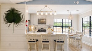 A kitchen with a central island, white cabinetry, and a hanging light fixture. - Gritz & Giggles, Southern Charm Meets Belly Laughs! Close to Parris Island (Port Royal)