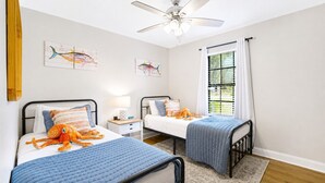 A bedroom with two beds, a ceiling fan, and artwork on the walls. - Gritz & Giggles, Southern Charm Meets Belly Laughs! Close to Parris Island (Port Royal)