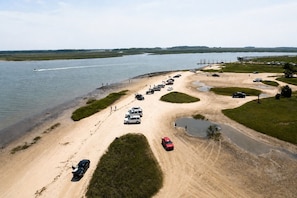 An aerial view of a parking area with vehicles, a sandy beach, and a body of water.
