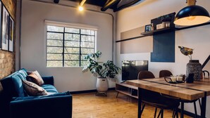 Ein modernes Wohnzimmer mit einem blauen Sofa, einem Holzespeisetisch und einem großen Fenster mit Blick auf Bäume.