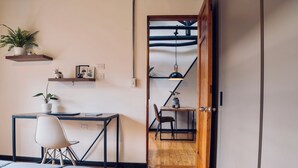 Ein Schlafzimmer mit Bett, Schreibtisch, Stuhl, einem Regal mit Pflanzen und einer Tür zu einem anderen Raum.