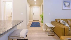 Una sala moderna con un sofá de cuero marrón, una mesita blanca pequeña y una zona de cocina con encimera de granito.