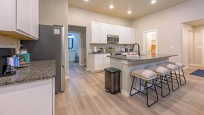 Una cocina moderna con armarios blancos, encimera de granito, una isla central con taburetes de bar, un refrigerador de acero inoxidable y un microondas.