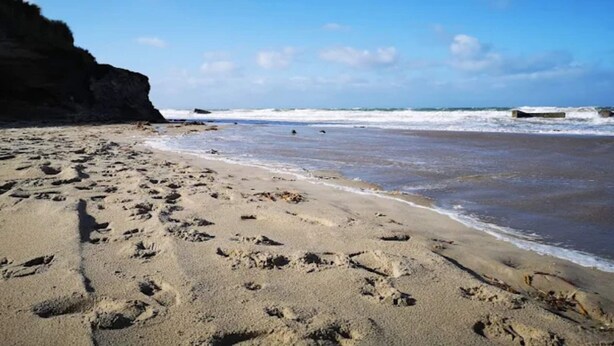 A sandy beach with footprints, a rocky cliff, and waves in the background. - 6 Person Holiday Home in Lokken (Lokken)
