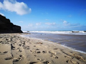 A sandy beach with footprints, a rocky cliff, and waves in the background. - 6 Person Holiday Home in Lokken (Lokken)