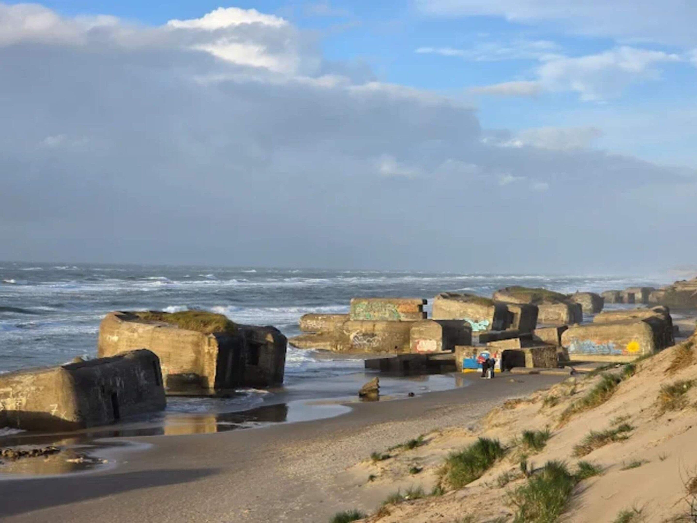 Une plage côtière avec de grandes structures en béton, une étendue de sable et l’océan en arrière-plan.