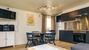 A compact kitchen with a modern stove, a dining area with a table and chairs, and a TV mounted on the wall. - 6 Person Holiday Home in Lokken (Lokken)