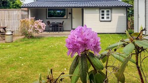 A single-story house with a tiled roof, a patio with a table and chairs, and a pink flower in the foreground. - 6 Person Holiday Home in Lokken (Lokken)
