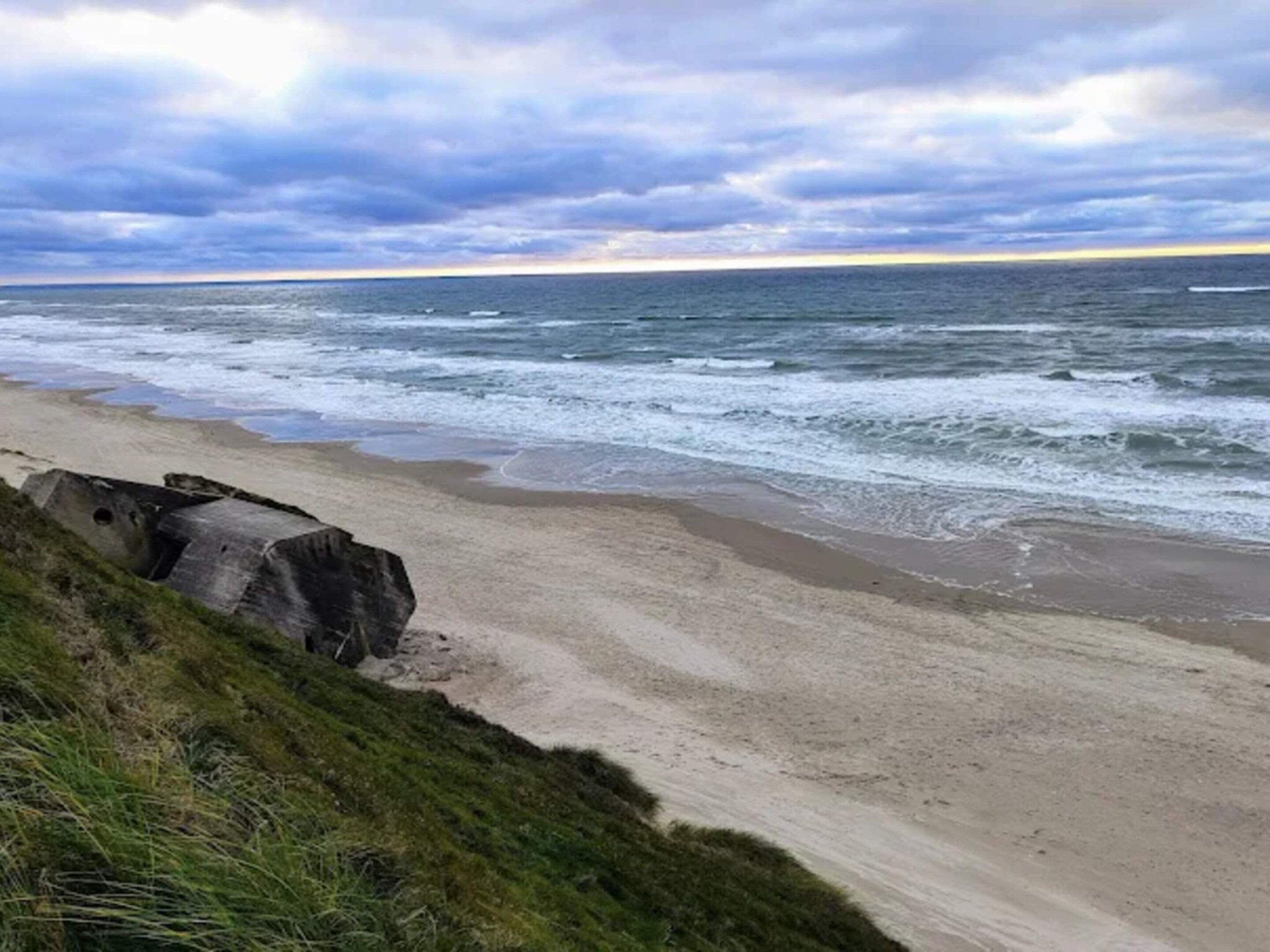 A beach with waves, a cloudy sky, and a concrete structure.