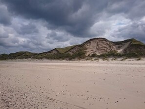 En strand med en stor klit og en truende himmel.