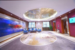 A hotel lobby with a large abstract painting, a circular carpet, seating area, and a television screen. - Yangling International Conference & Exhibition Center Hotel (Xianyang)