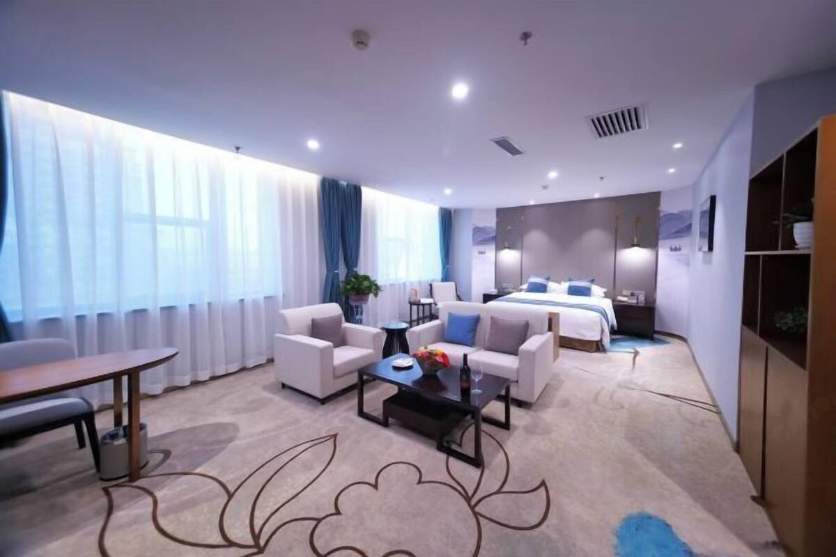 A hotel room with a bed, two sofas, a coffee table, a desk, and a large window with curtains.