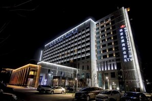 Un hotel de varios pisos con fachada moderna, señalización iluminada y un estacionamiento con varios automóviles.