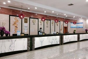 Zona de recepción de un hotel con mostrador de mármol, detalles decorativos rojos y una recepcionista.