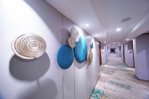 A hotel hallway with a patterned carpet, wall-mounted decorative items, and a long corridor leading to rooms.