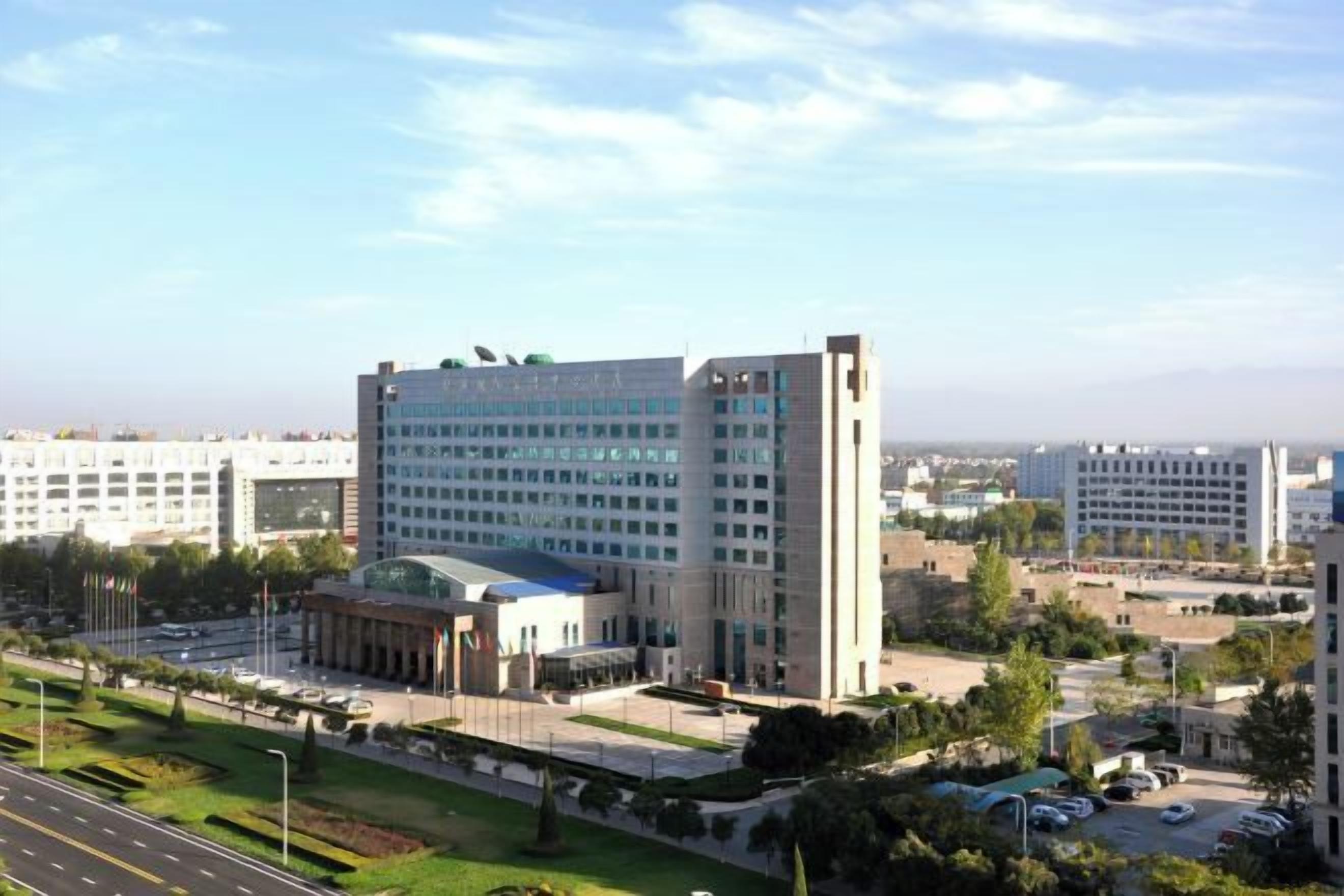 A multi-story building with a central courtyard, surrounded by greenery and a parking area.