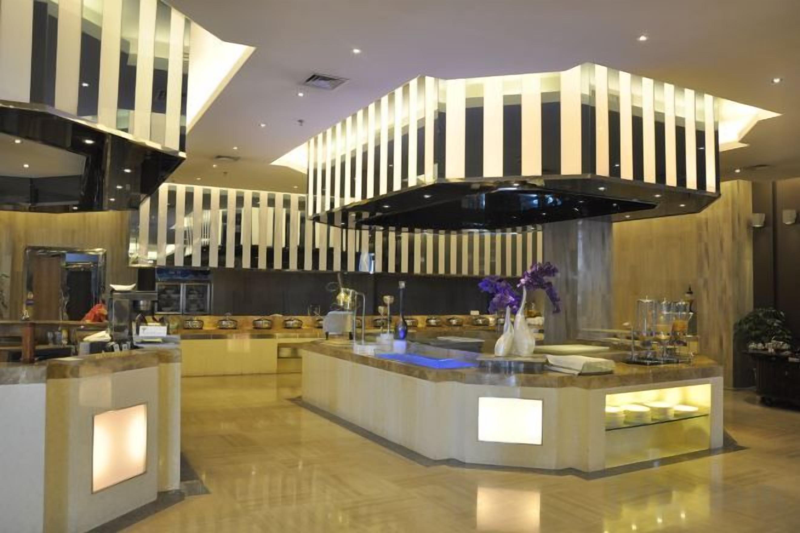 A modern hotel lobby with a central reception desk, a large black and white striped ceiling design, and a marble floor.