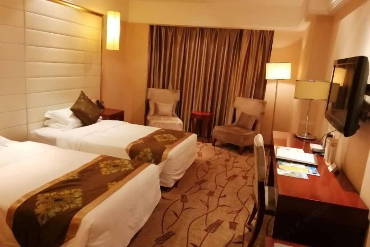 A hotel room with two beds, a desk, a chair, a TV, and a curtain.