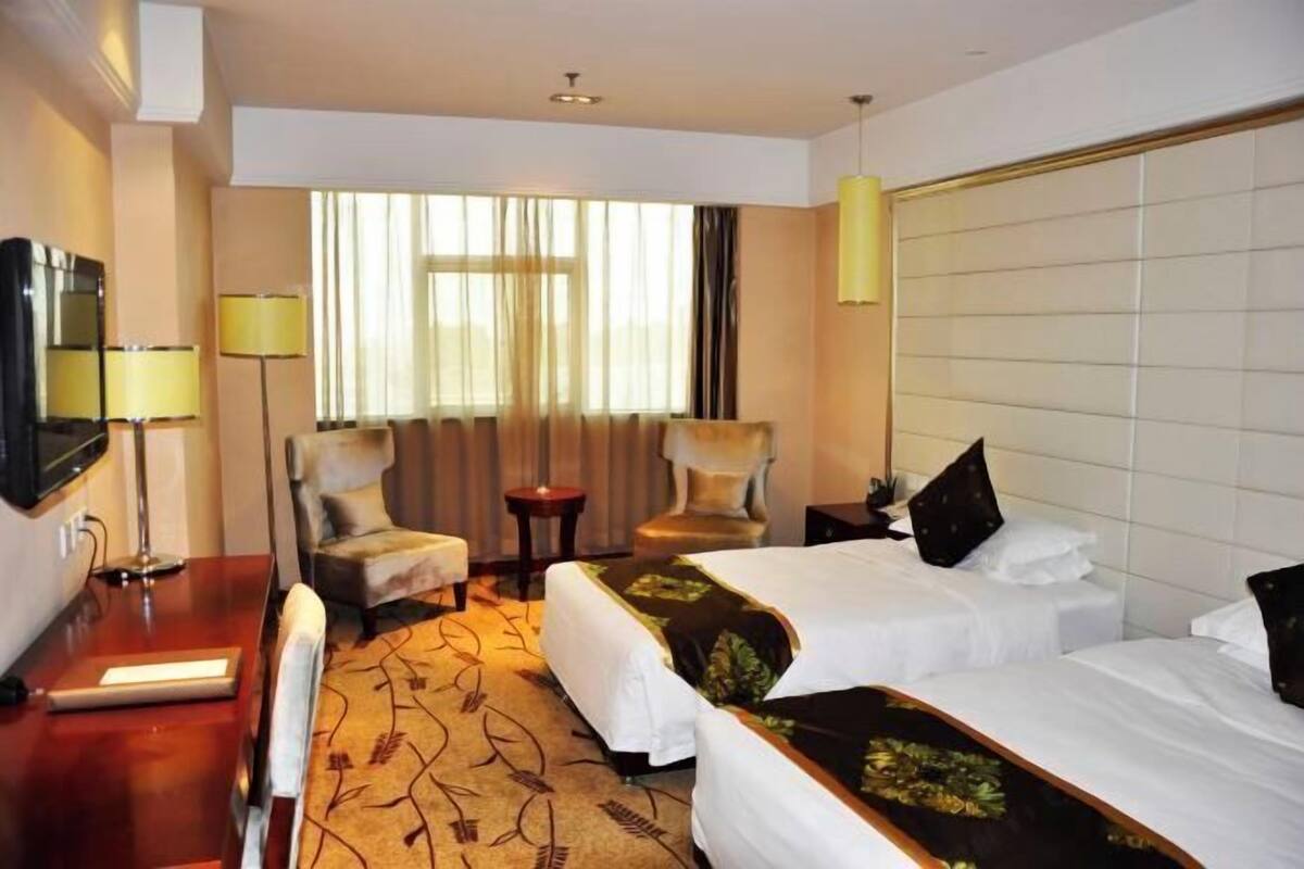A hotel room with two beds, a desk, a chair, a TV, and a window with curtains.